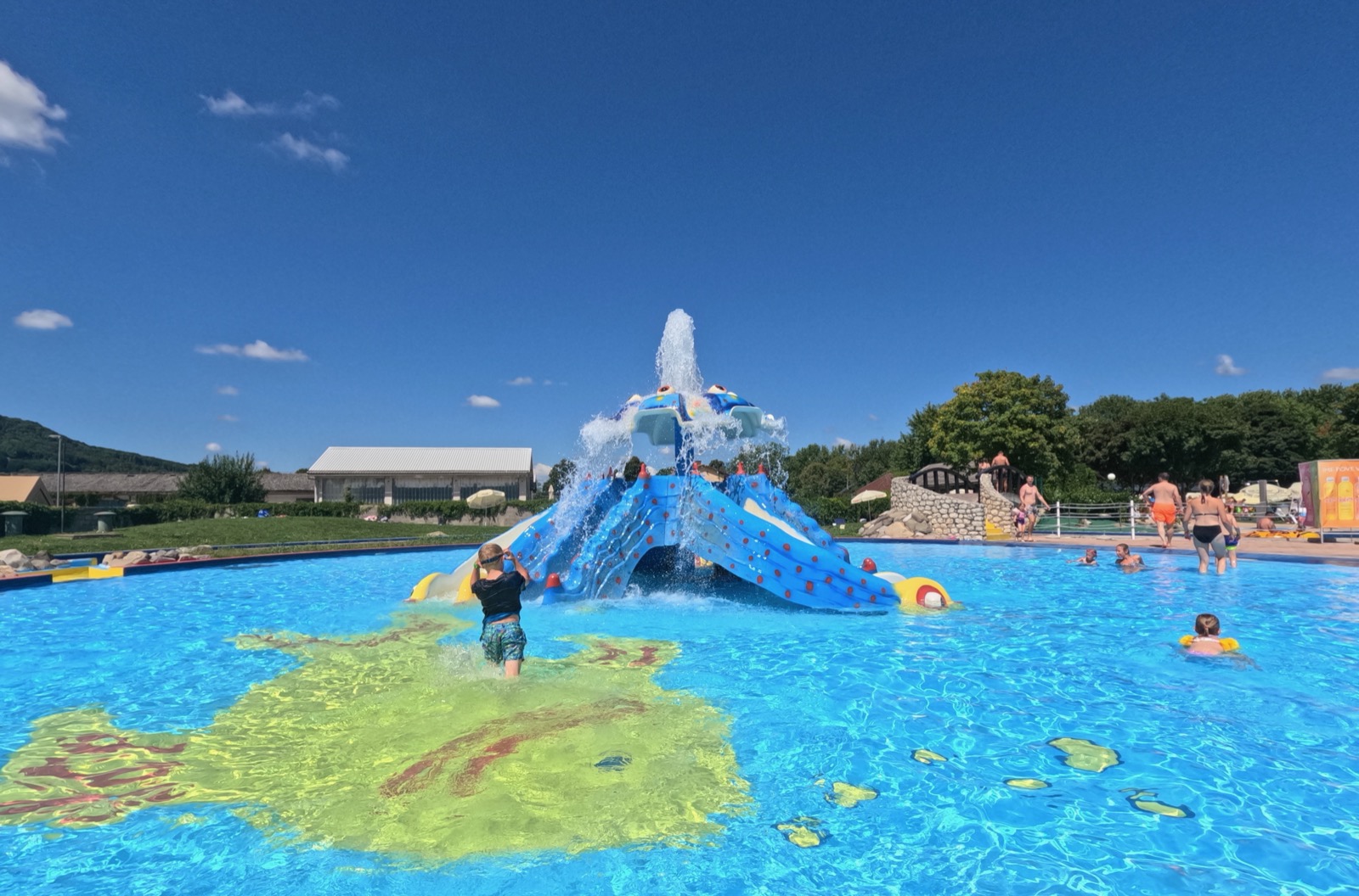 Children playing in a swimming pool with a water slide and a fake island.